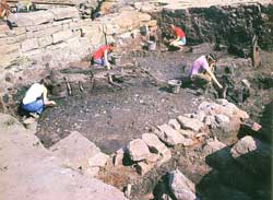 Excavations  in progress on pre-Hadrianic fort. The stone walls belong to later buildings. Timber posts and fencing are visible, well preserved in the anaerobic conditions