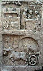 Scene on a 2nd / 3rd century AD funerary monument from Trier.
An ox pulls a cart bearing a large wine barrel.  In the panel above, a barrel and an olive oil amphora wrapped in rope, in front of a counter.
